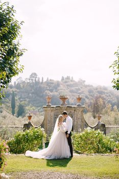 Wedding at an old winery villa in Tuscany, Italy. Round wedding arch decorated with white flowers and greenery in front of an ancient Italian architecture. The bride and groom walk in the park.