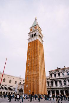 A huge bell tower made of red brick in Piazza San Marco in Venice, Italy. Against background of a cloudy, evening, October sunset sky.