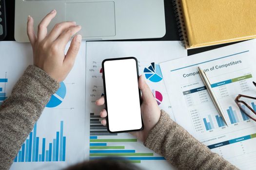 Top view of business woman using smartphone with blank white screen and laptop computer for accounting and financial, work at home