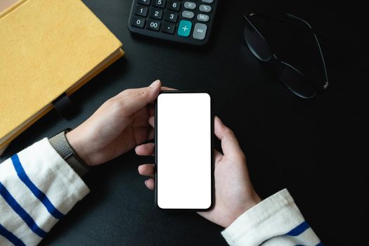 Top view of woman holding blank screen smartphone in dark trendy workspace.