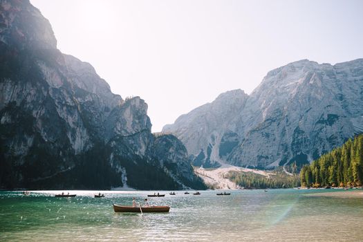 Newlyweds swim in a wooden boat on Lago di Braies in Italy. Wedding in Europe, at Braies lake. Wedding couple - Groom rows wooden oars, the bride sits opposite.