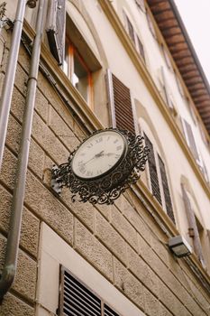 Vintage street clock on the wall of the building, with metal forged decoration.