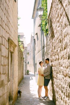 A man and a woman hugging at a white brick wall in a narrow alley of the old town of Perast . High quality photo