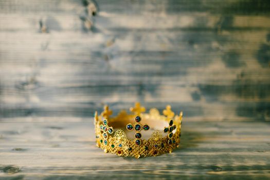 Golden crown encrusted with precious stones for wedding in the church, against a wooden background