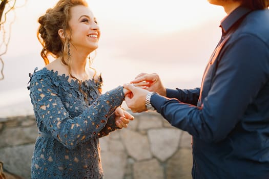 The groom puts the ring on the bride's finger at sunset during the wedding ceremony, the bride smiles . High quality photo