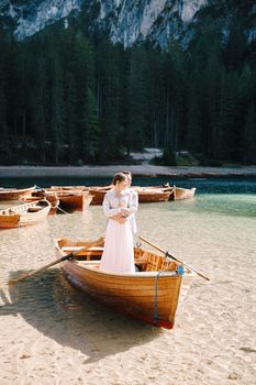 The bride and groom in a wooden boat at Lago di Braies in Italy. Wedding couple in Europe, at Braies lake. The newlyweds stand in the boat and cuddle.