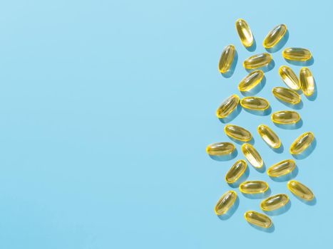 Vitamin D3, Omega or Evening Primrose Oil gel capsules on blue background. Top view or flat lay yellow liquid capsules with nutritional supplement oil. Copy space for text.