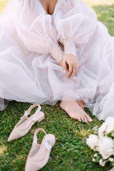 Wedding in Florence, Italy, in an old villa-winery. Barefoot legs of the bride on the grass, next to shoes and bouquet.