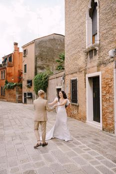 The bride and groom walk through the deserted streets of the city. Newlyweds hug, dance, hold hands against the backdrop of picturesque red brick houses.