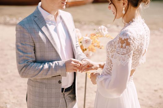 The groom dons a bride's ring, in place for the ceremony, with an arch of autumn floral columns, against the backdrop of Lago di Braies in Italy. Destination wedding in Europe, at Braies lake.