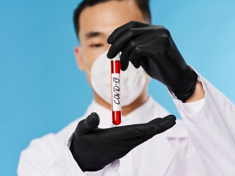 A man of Asian appearance in a protective mask blood test black gloves diagnostics blue background. High quality photo