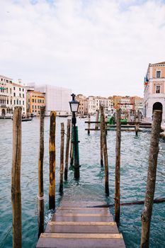 Wooden pier for boats and gondolas in Italy, in Venice. Wooden staircase goes under water, vertical piles of tree trunks. Grand canal with azure-colored sea water