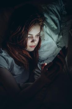 woman with a phone in her hands at night lying in bed rest before bedtime. High quality photo