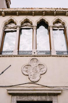 Four Venetian windows with a reflection of the sky in the glass. Windows with a sharp top, with rag rollers outside, small forged windowsills.
