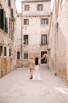 The bride and groom walk through the deserted streets of the city. Newlyweds walk in a dead-end alley against the background of brick buildings.