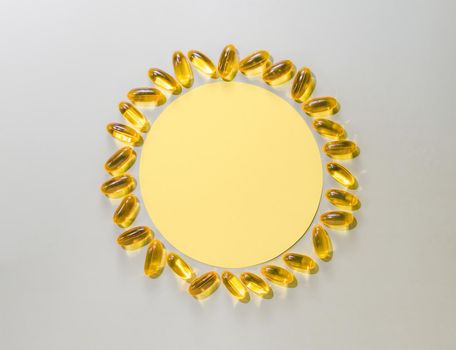 Vitamin D3 liquid capsules around yellow circle on neutral gray background. Top view or flat lay yellow sun made with paper circle and liquid capsules with copy space.