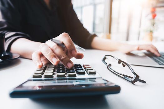 Close up Business woman using calculator and laptop for do math finance on wooden desk in office and business working background, tax, accounting, statistics and analytic research concept