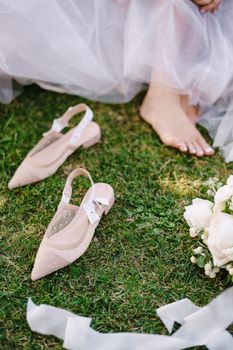 Wedding in Florence, Italy, in an old villa-winery. Barefoot legs of the bride on the grass, next to shoes and bouquet.
