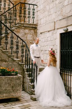 The bride and groom stand on a narrow staircase with a beautiful wrought railing in the old city of Kotor. High quality photo