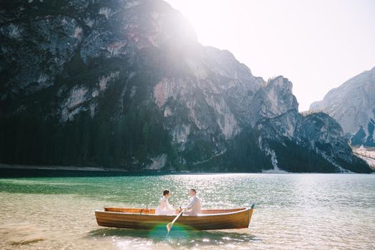 Newlyweds swim in a wooden boat on Lago di Braies in Italy. Wedding in Europe, at Braies lake. Wedding couple - Groom rows wooden oars, the bride sits opposite.