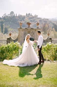 Wedding at an old winery villa in Tuscany, Italy. Round wedding arch decorated with white flowers and greenery in front of an ancient Italian architecture. The bride and groom walk in the park.