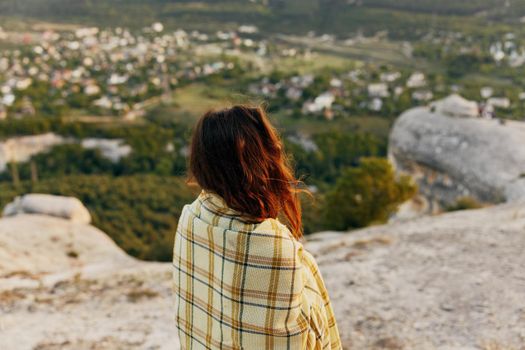 red-haired woman with a plaid on her shoulders looks at the village in the distance. High quality photo