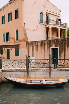 Boats moored at the walls of a building in canal in Venice, Italy. Classic Venetian street views - wooden shutters, brick houses, bridges