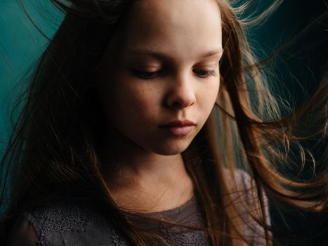 Sad girl with disheveled hair on a turquoise background in a gray dress. High quality photo