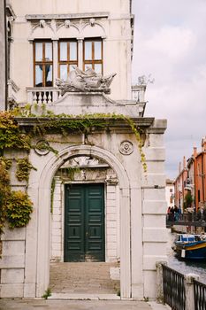 Beautiful stone arched entrance to the building, green door and classic Venetian windows. Details of the facades of buildings on the streets of Venice, Italy.
