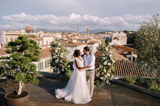 Interracial wedding couple. Destination fine-art wedding in Florence, Italy. A wedding ceremony on the roof of the building, with cityscape views of the city and Cathedral of Santa Maria Del Fiore