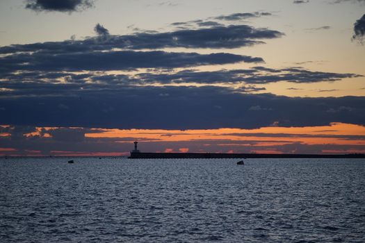 Sunset in the sea Bay on the payroll of the dark sky and Cape with a shining lighthouse