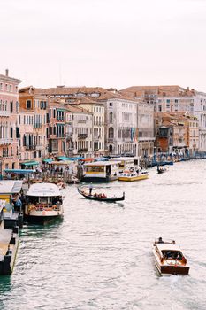 Grand Canal Embankment in Venice, Italy. Near the Rialto Bridge. People ride beautiful wooden motor boats, gondoliers carry tourists, large ships with people stand at the pier.