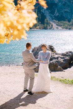 Bride and groom under autumn tree with fiery yellow foliage at Lago di Braies in Italy. Destination wedding in Europe, at Braies lake. In love, the newlyweds dance and whirling.