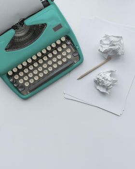 A blue vintage typewriter with paper sheets, stencil and paper balls on white background.
