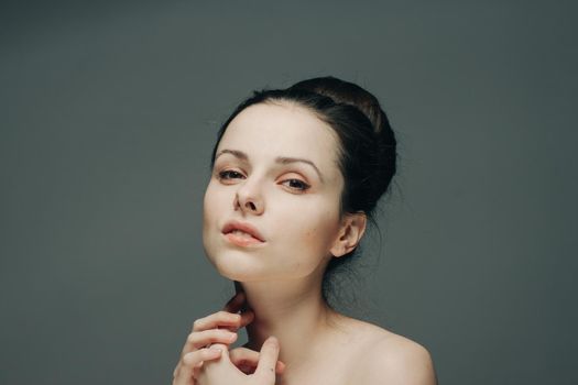 nude woman with hairstyles in her head touches her face with her hands on a gray background. High quality photo