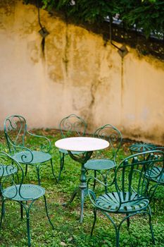 White small cocktail table surrounded by six green forged metal chairs in front of a cement wall at Medici Villa of Lilliano Wine Estate in Tuscany, Italy.