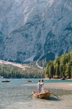 Bride and groom sailing in wooden boat, with oars at Lago di Braies lake in Italy. Wedding in Europe - Newlyweds are standing embracing in boat