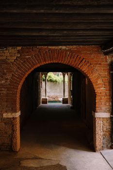 View from the building on to a small narrow canal between houses in Venice, Italy. A view from tunnel with brick walls, two antique columns and water in the sea.