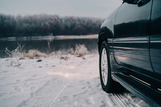 black car near the river on a snowy road and forest in the background. High quality photo