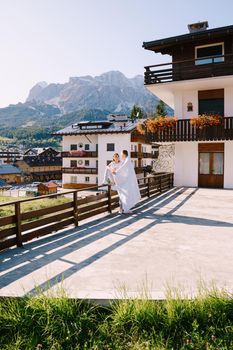 A guy and a girl cuddle with a blanket outside a hotel in mountains. Cortina Ampezzo is an Italian city in province of Belluno in Veneto region, a winter resort in Dolomites