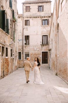 The bride and groom walk through the deserted streets of the city. Newlyweds walk in a dead-end alley against the background of brick buildings.