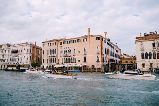 Tourists on the waterfront in Venice, against the background of the ancient facades of buildings standing in water. Water sightseeing in Venice, Italy.