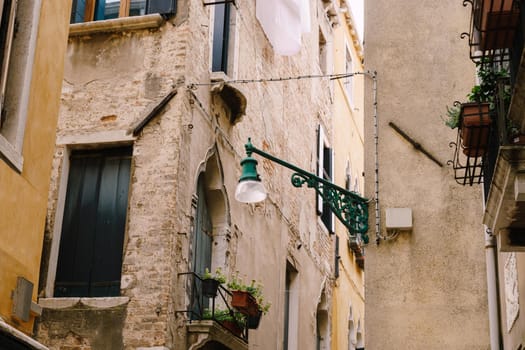 An ancient street lamp, on the corner of the front of the house, on the street in Venice, Italy.