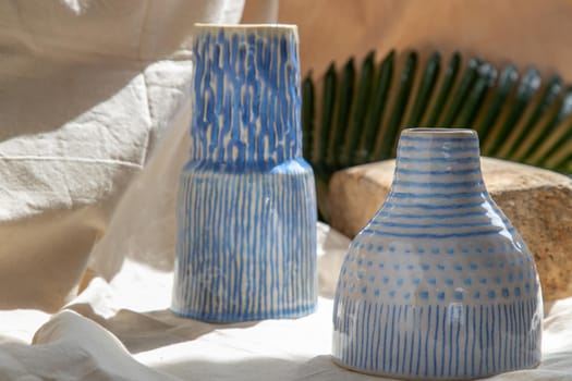 Two white and blue handmade ceramic vases on white textured table cloth.  Home decor, Copy space, Selective focus.