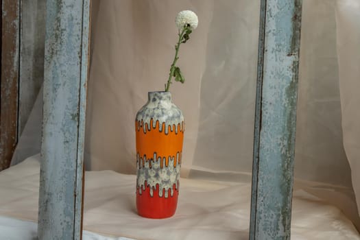 White flower in Orange and Red handmade ceramic vase on Blush textured table cloth. Home decor, Copy space, Selective focus.