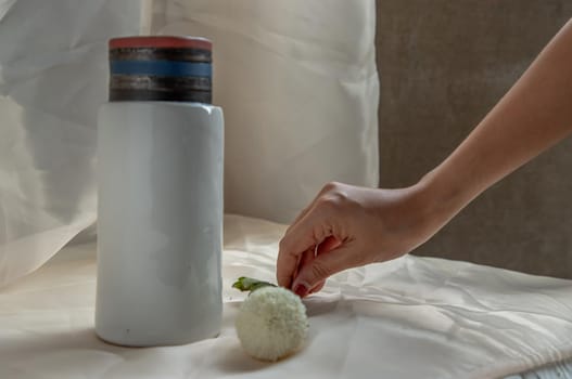 Hands of a young woman with White flower and handmade ceramic vase and on Blush textured table cloth. Home decor, Copy space, Selective focus.