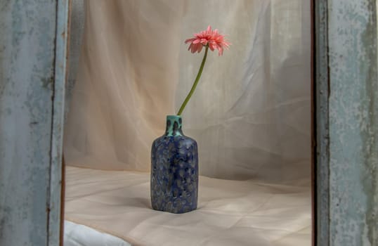 Pink flower in Blue handmade ceramic vase on Blush textured table cloth. Home decor, Copy space, Selective focus.