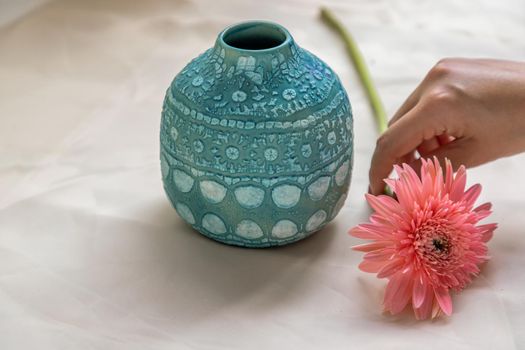 Hands of a young woman with Pink flower and handmade ceramic vase and on Blush textured table cloth. Home decor, Copy space, Selective focus.