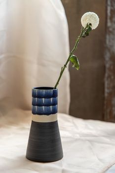 White flower in Blue handmade ceramic vase and on Blush textured table cloth. Home decor, Copy space, Selective focus.