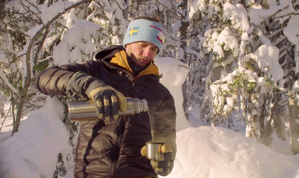 Young man pouring hot tea from a thermos in winter